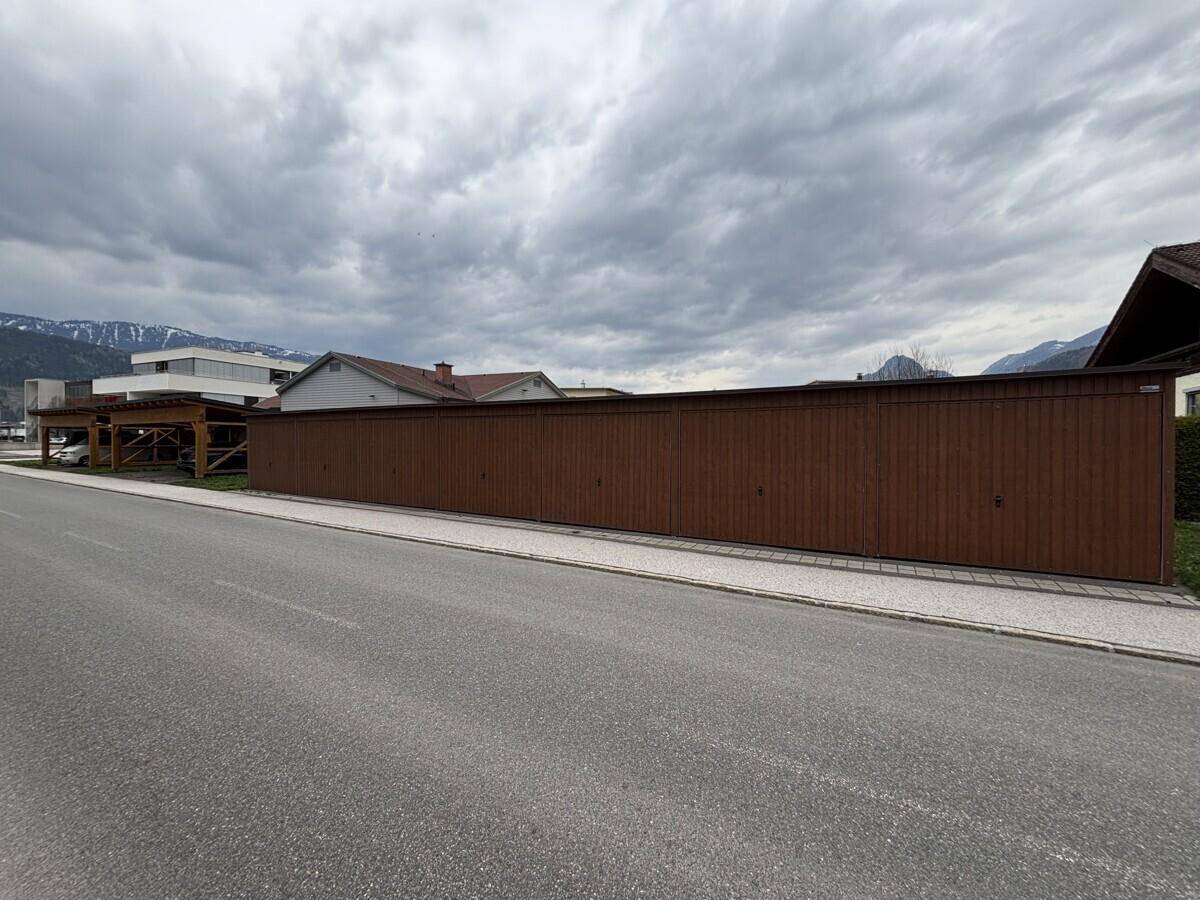 Lange Reihe von Garagen mit braunen Holztoren entlang einer Straße, umgeben von Bergen.