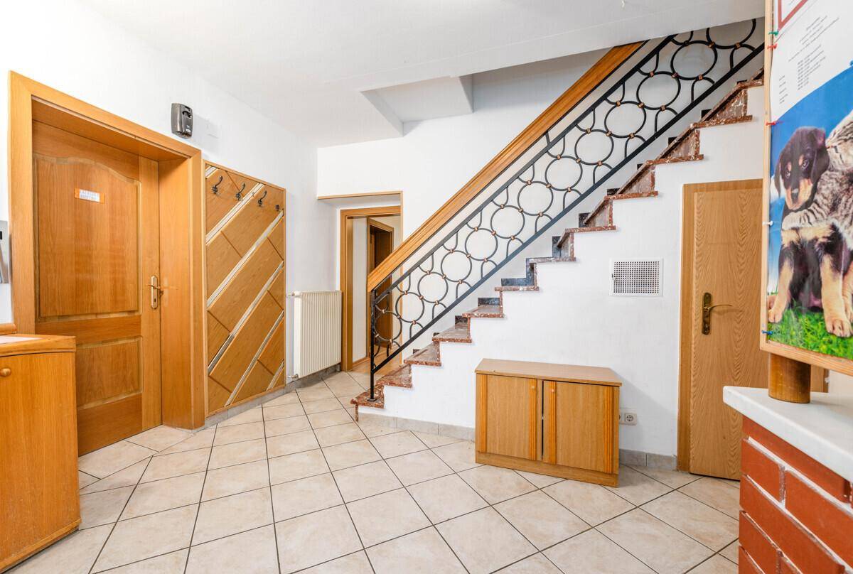 Heller Eingangsbereich mit gefliestem Boden, Holzmöbeln und einer Treppe mit schmiedeeisernem Geländer.