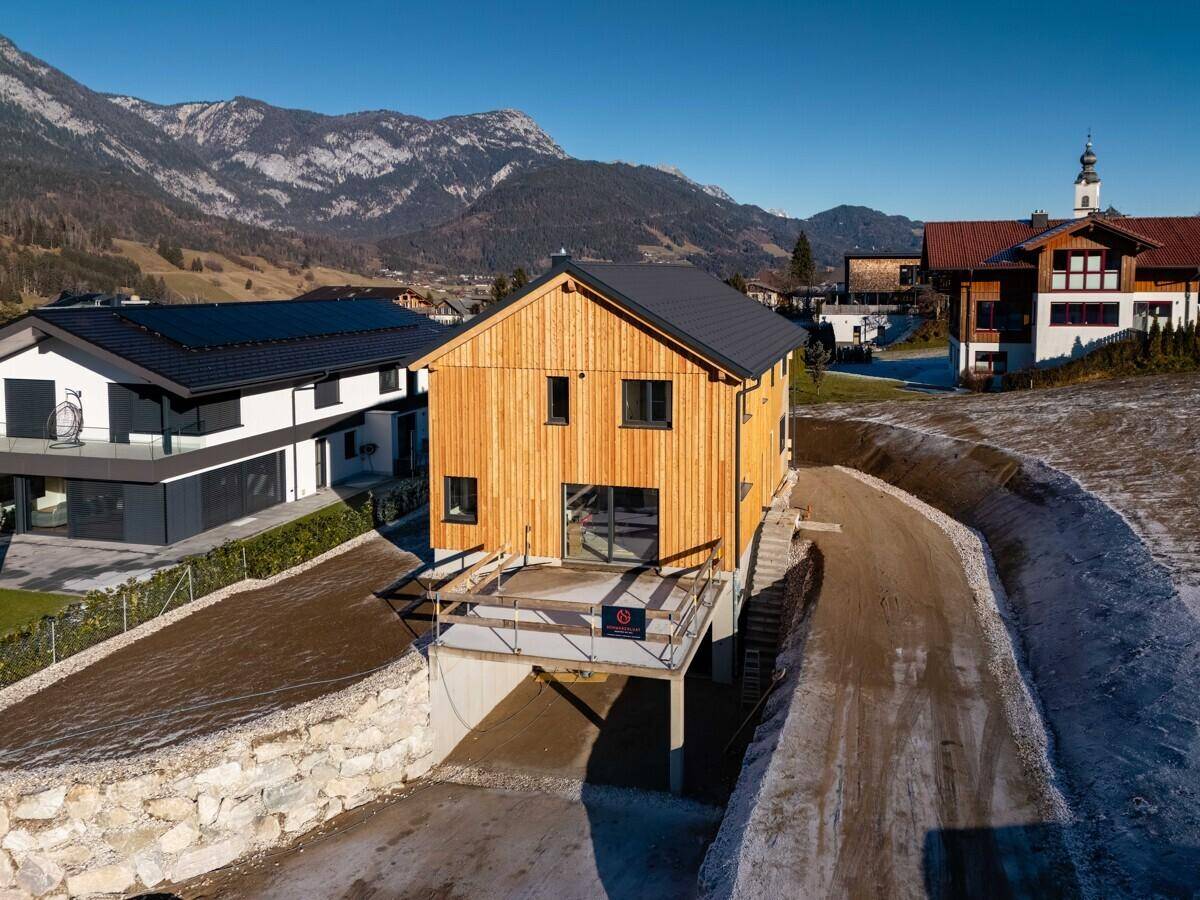 Modernes Holzhaus mit dunklem Dach und Bergblick in ländlicher Umgebung.