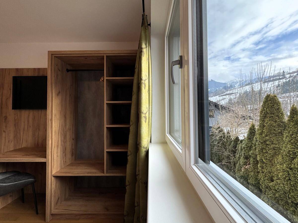 Fensterblick aus dem Schlafzimmer auf die verschneite Berglandschaft und grüne Bäume.