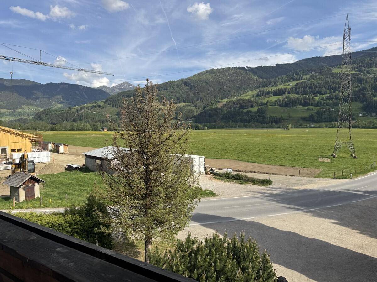 Weitläufiger Ausblick vom Balkon über grüne Felder, eine Straße und die umliegenden Berge.