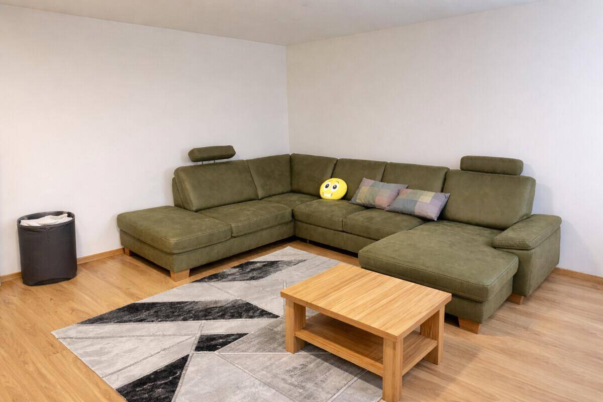 Wohnzimmer mit großem grünen Ecksofa, Couchtisch und Holzboden.