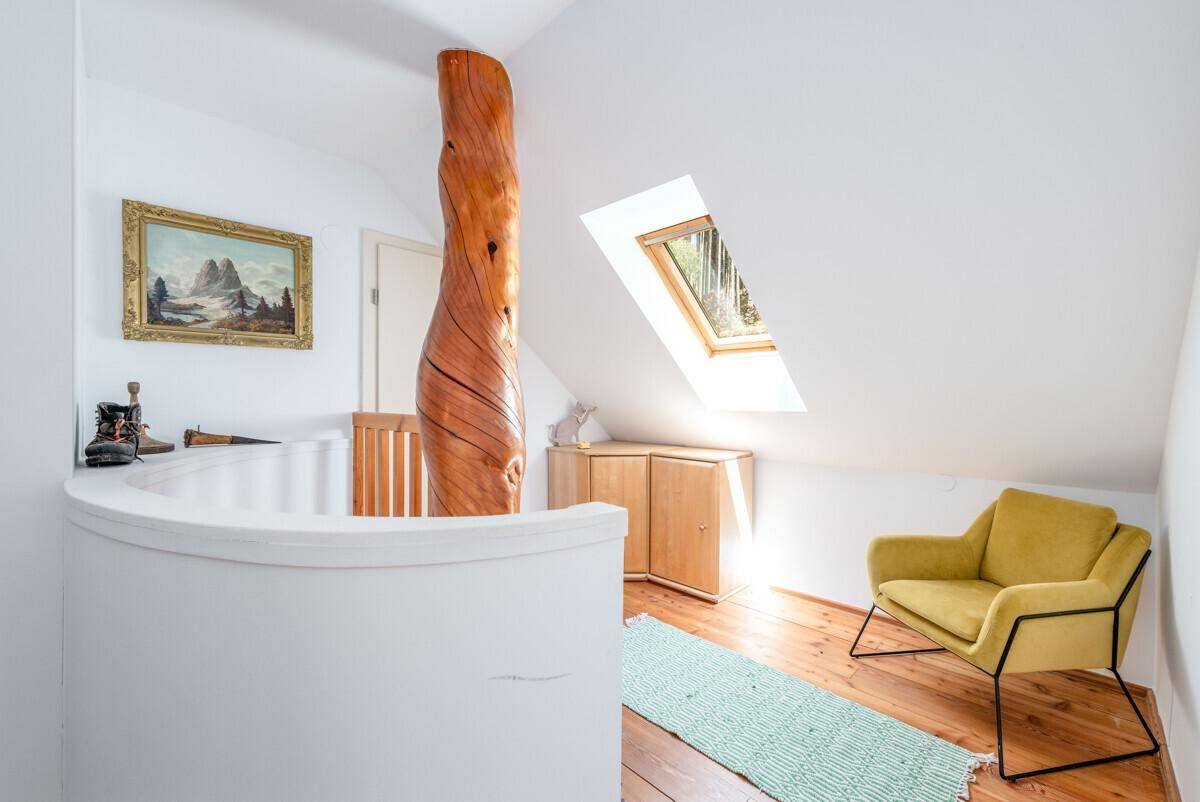 Heller Dachbodenbereich mit einzigartigem Holzpfosten, gemütlichem Sessel und Dachfenster.