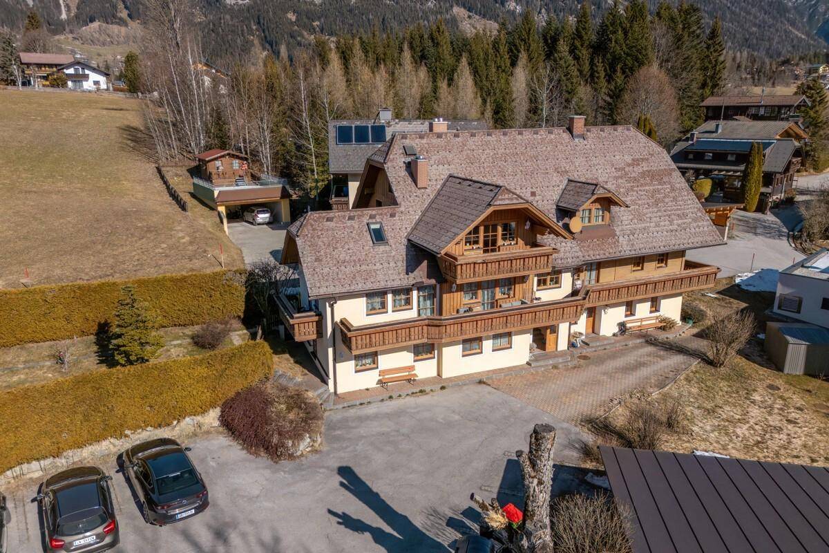 Luftaufnahme eines traditionellen Gebäudes mit Satteldach, umgeben von Natur und Parkplätzen.