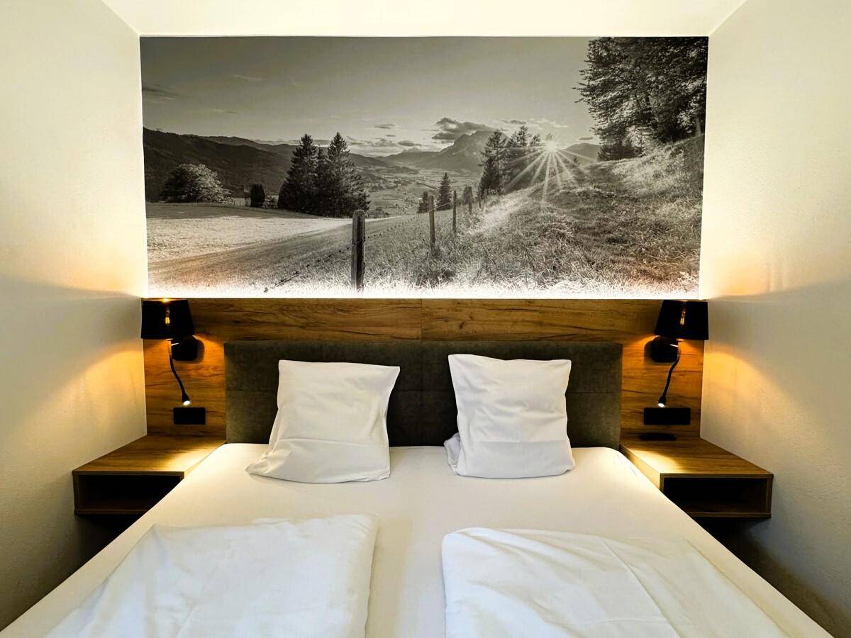 Schlafzimmer mit Doppelbett, Holzkopfteil und Wandtapete mit Sonnenaufgang über der Landschaft.