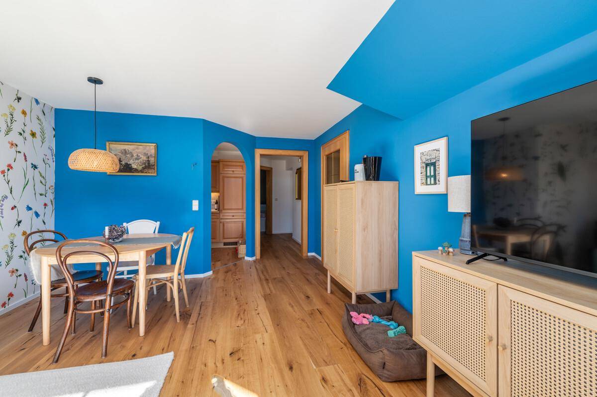 Offener Wohn-Essbereich mit blauen Wänden, Holzboden und Zugang zur Küche.