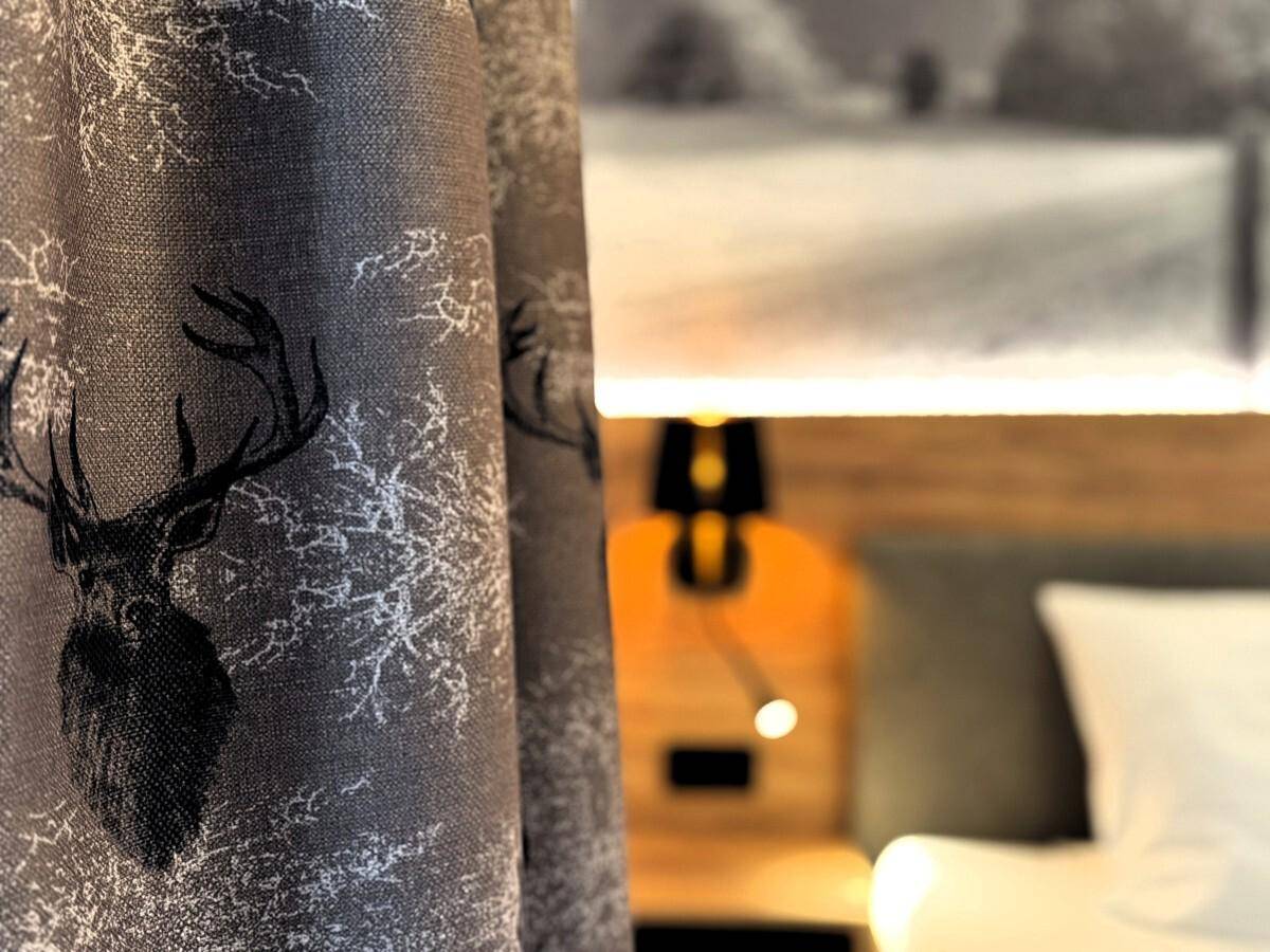 Detailansicht des Vorhangs mit Hirschmotiv und der Bettwäsche im Schlafzimmer.