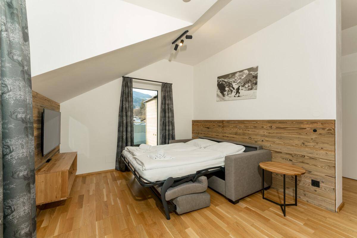 Wohnzimmer mit ausziehbarem Schlafsofa, Holzwandverkleidung und Blick auf die Berge.