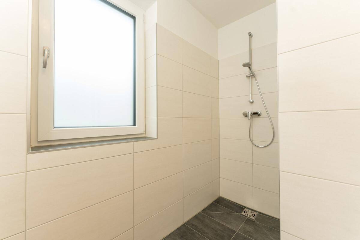 Duschbereich im Badezimmer mit hellen Wandfliesen und Fenster für Tageslicht.