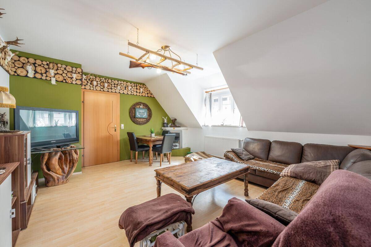 Wohn- und Essbereich mit Sofa, Fernseher und grüner Akzentwand mit Holzscheit-Dekoration.