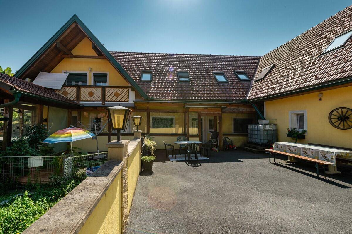 Außenbereich mit gepflasterter Fläche, Gartenmöbeln und einem Sonnenschirm vor dem Gebäude.