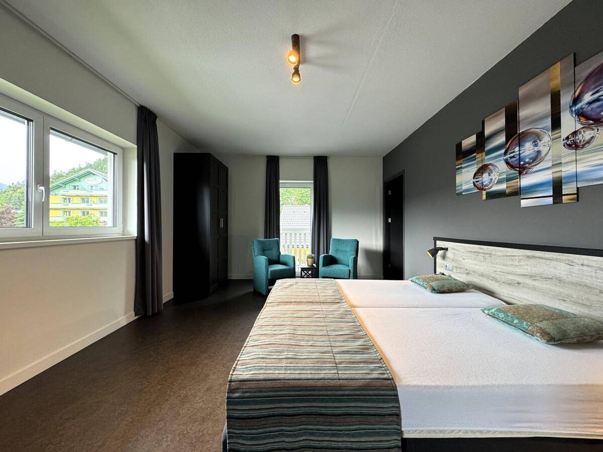 Helles Schlafzimmer mit zwei Einzelbetten, Schrank und Fenstern mit Blick ins Grüne.