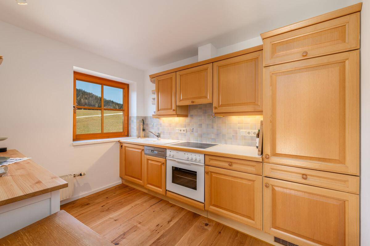 Funktionale Küche mit Holzschränken, Einbaugeräten und Fenster mit Blick ins Grüne.