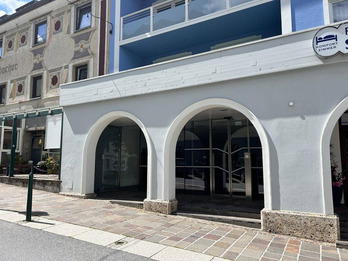 Gebäudefassade mit modernen blauen Balkonen und traditionellen Bögen im Erdgeschoss, an einer belebten Straße gelegen.