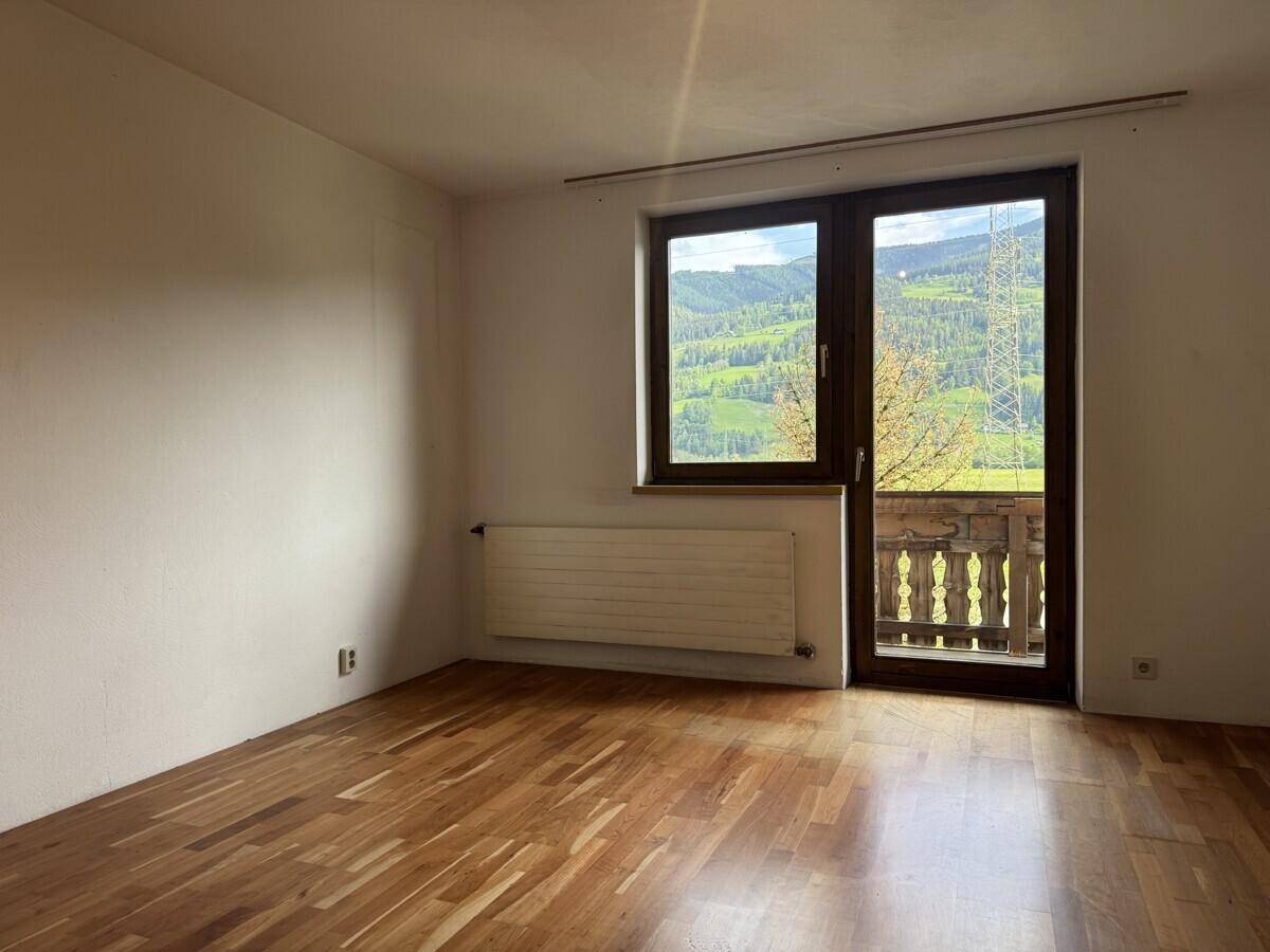 Geräumiges Zimmer mit Laminatboden, Balkonzugang und weitem Blick auf die Berglandschaft.