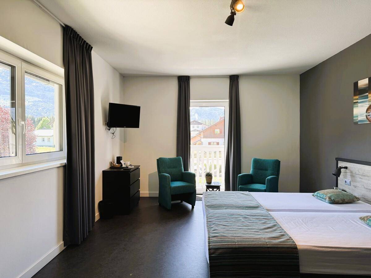 Schlafzimmer mit zwei Einzelbetten, Fernseher und Fenstern mit Blick ins Grüne.