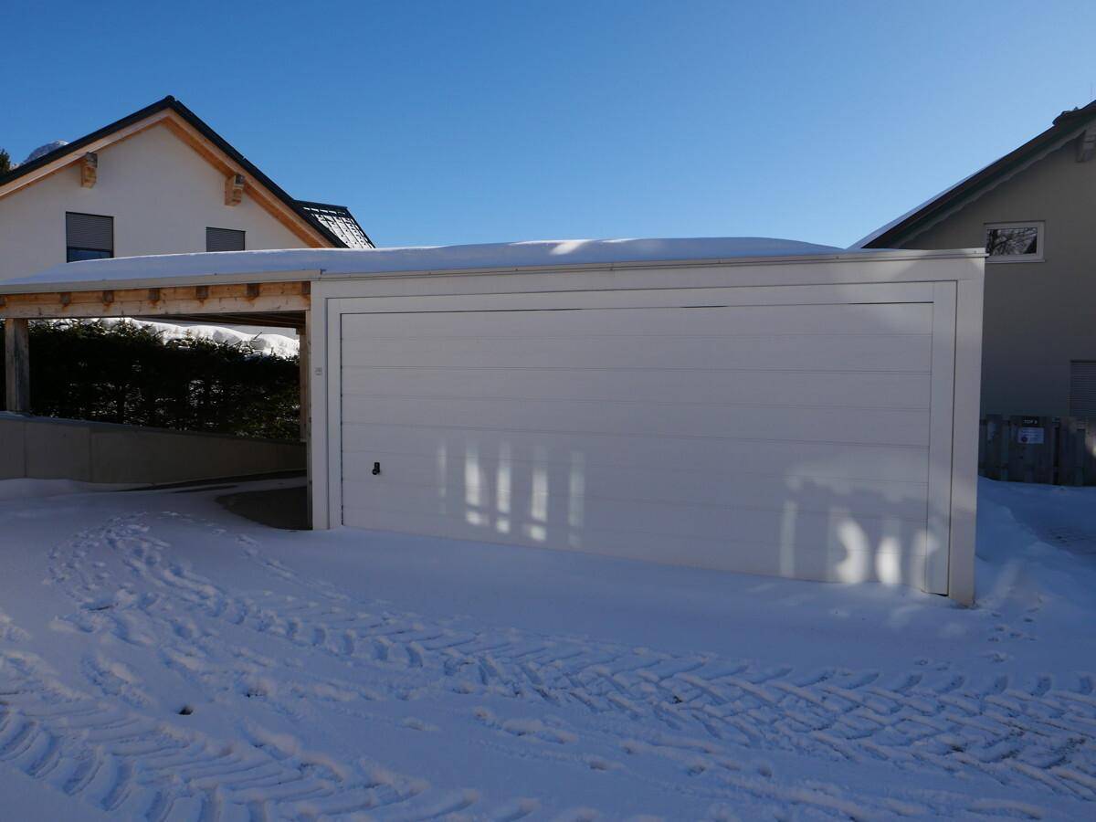 Ansicht der modernen Garage und des Carports mit Schnee auf dem Vorplatz an einem sonnigen Tag.