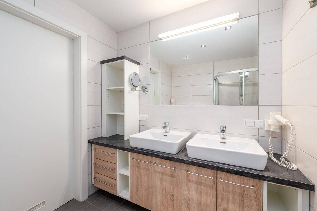 Modernes Badezimmer mit Doppelwaschbecken, großem Spiegel und Duschkabine im Hintergrund.