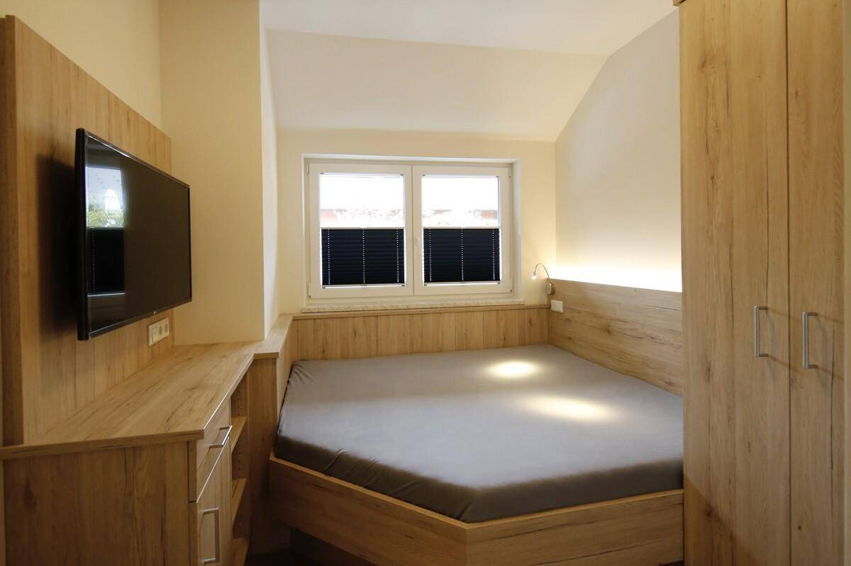Schlafzimmer mit einzigartigem Bettrahmen, Holzmöbeln und einem Fenster unter der Dachschräge.