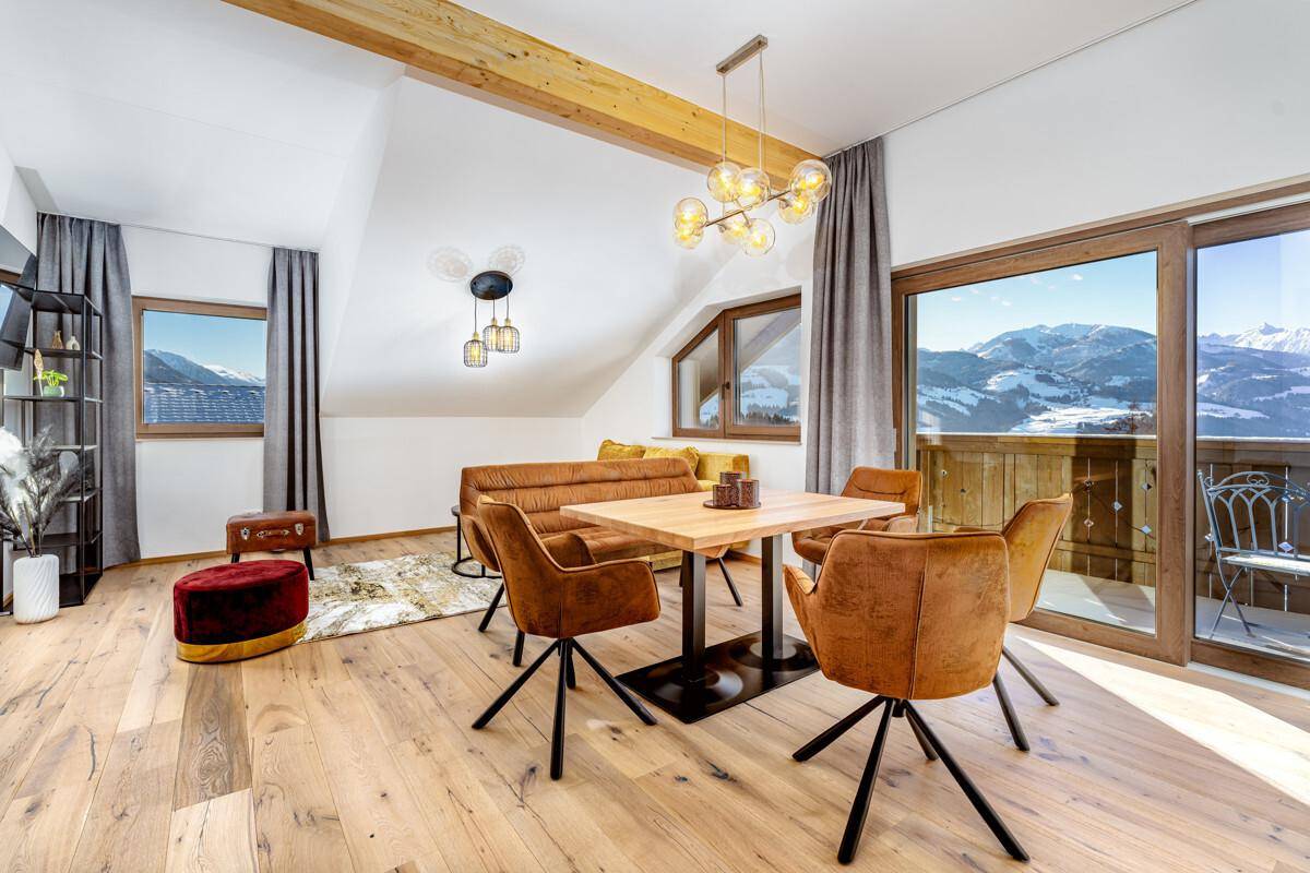 Geräumiger Wohnbereich mit Holzbalken, Dachschräge und weitem Blick auf die Berglandschaft.
