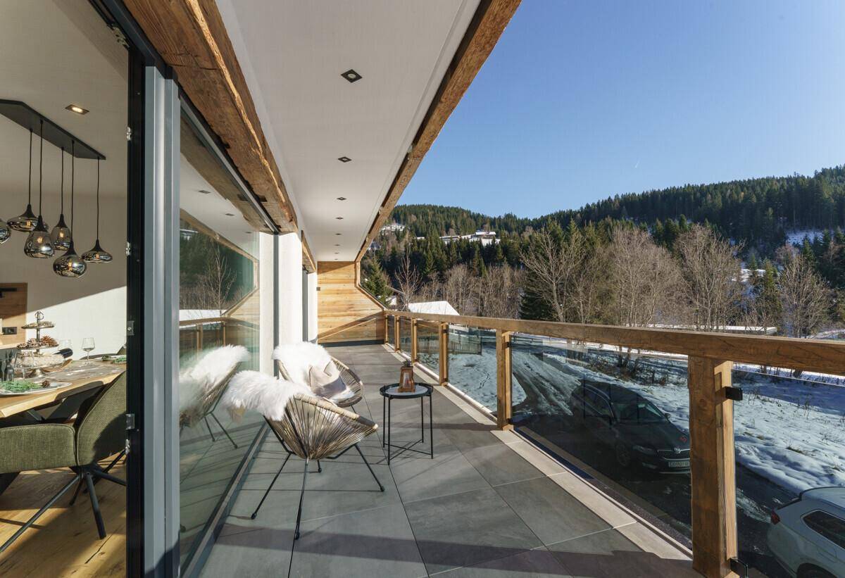 Geräumiger Balkon mit Glasgeländer, Sitzgelegenheiten und Panoramablick auf die Berge.