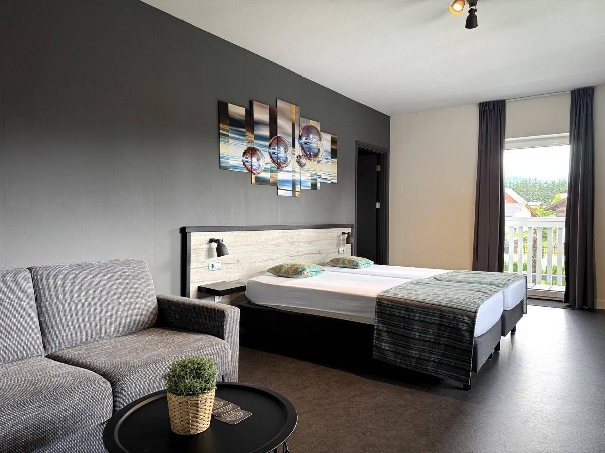Schlafzimmer mit Doppelbett, Sofa und Balkonzugang, modern eingerichtet.