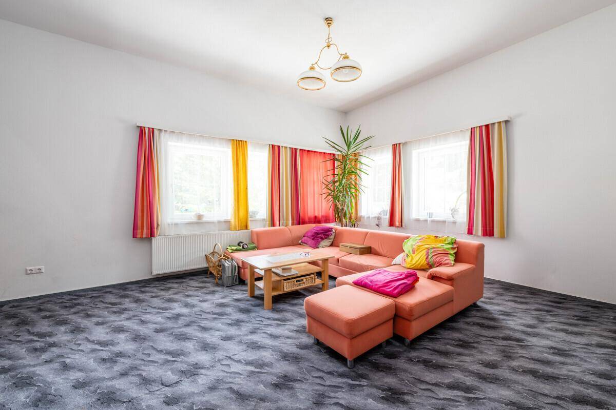 Geräumiges Wohnzimmer mit großem korallfarbenem Sofa, bunten Vorhängen und gemustertem Boden.