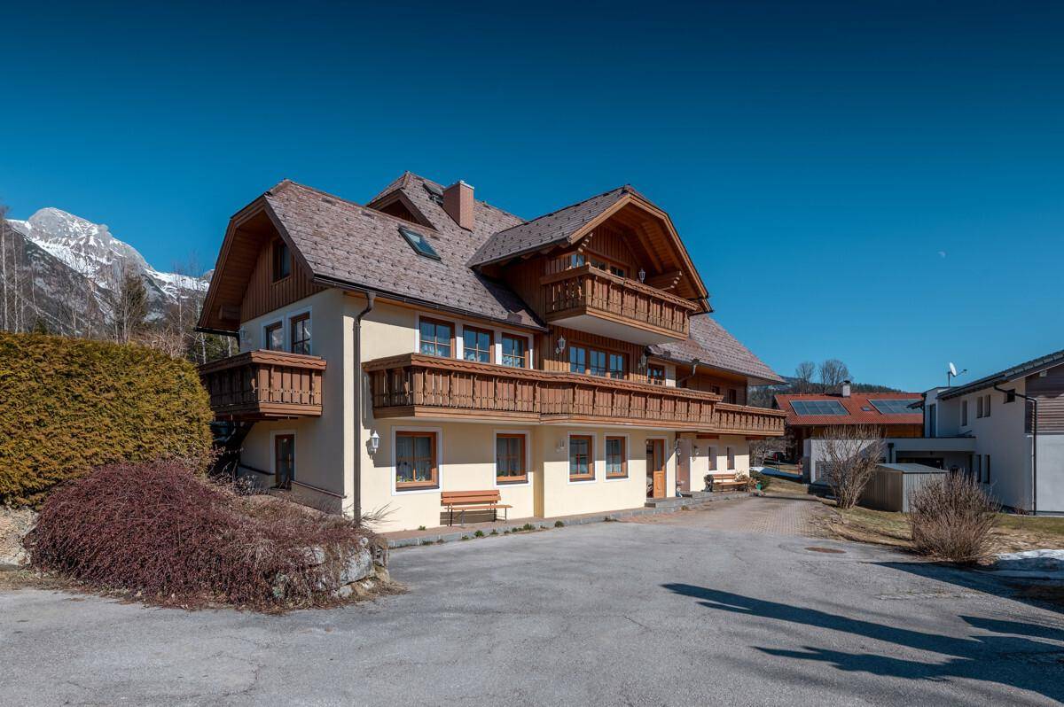 Traditionelles Haus mit Holzbalkonen und Bergblick unter blauem Himmel.