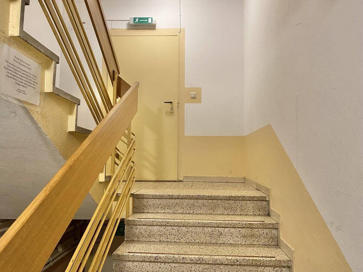 Treppenhaus mit Terrazzostufen und gelbem Geländer, das zu den oberen Etagen führt.