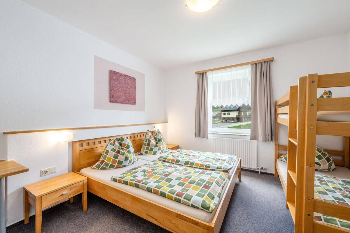 Schlafzimmer mit Doppelbett, Etagenbett und Fenster, ideal für Familien oder Gruppen.