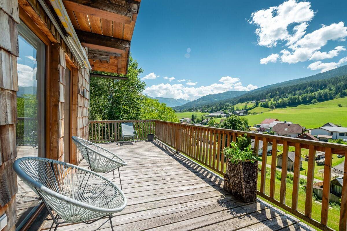 Geräumiger Holzbalkon mit Sitzgelegenheiten und weitem Blick über das Tal und die Berge.