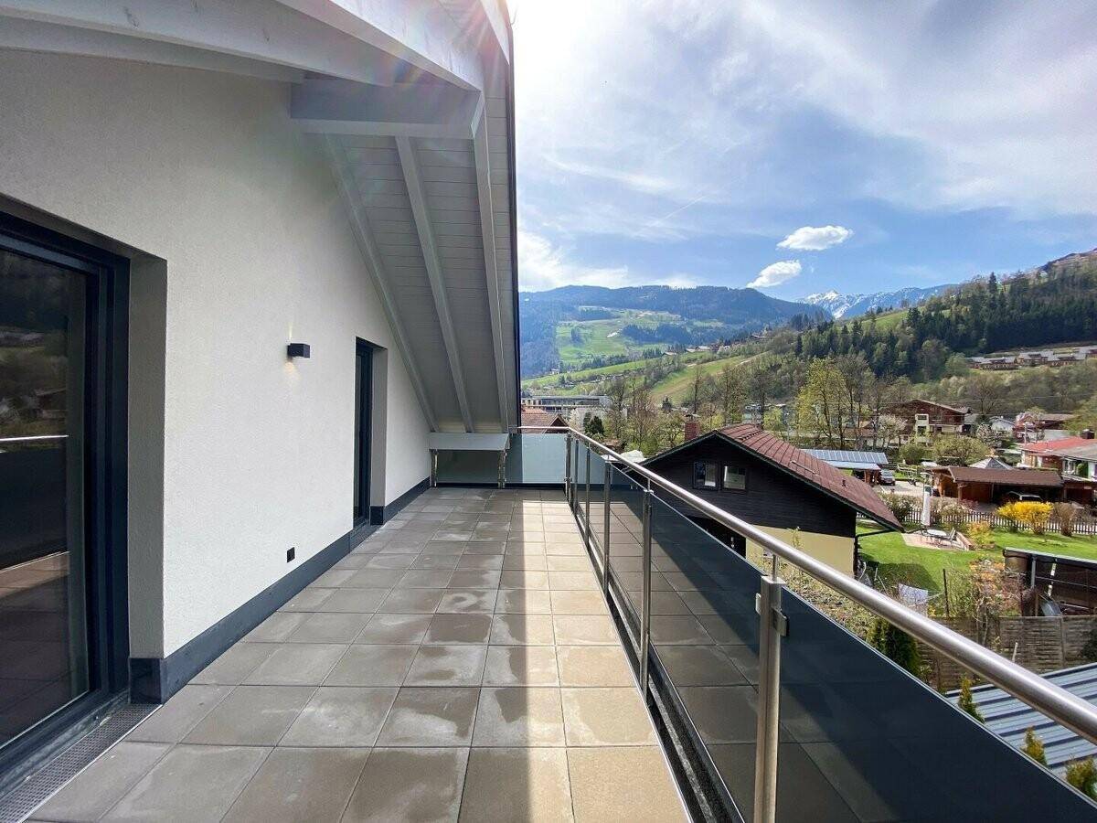 Großer Balkon mit Glasgeländer, Fliesenboden und weitem Blick auf die grüne Landschaft.