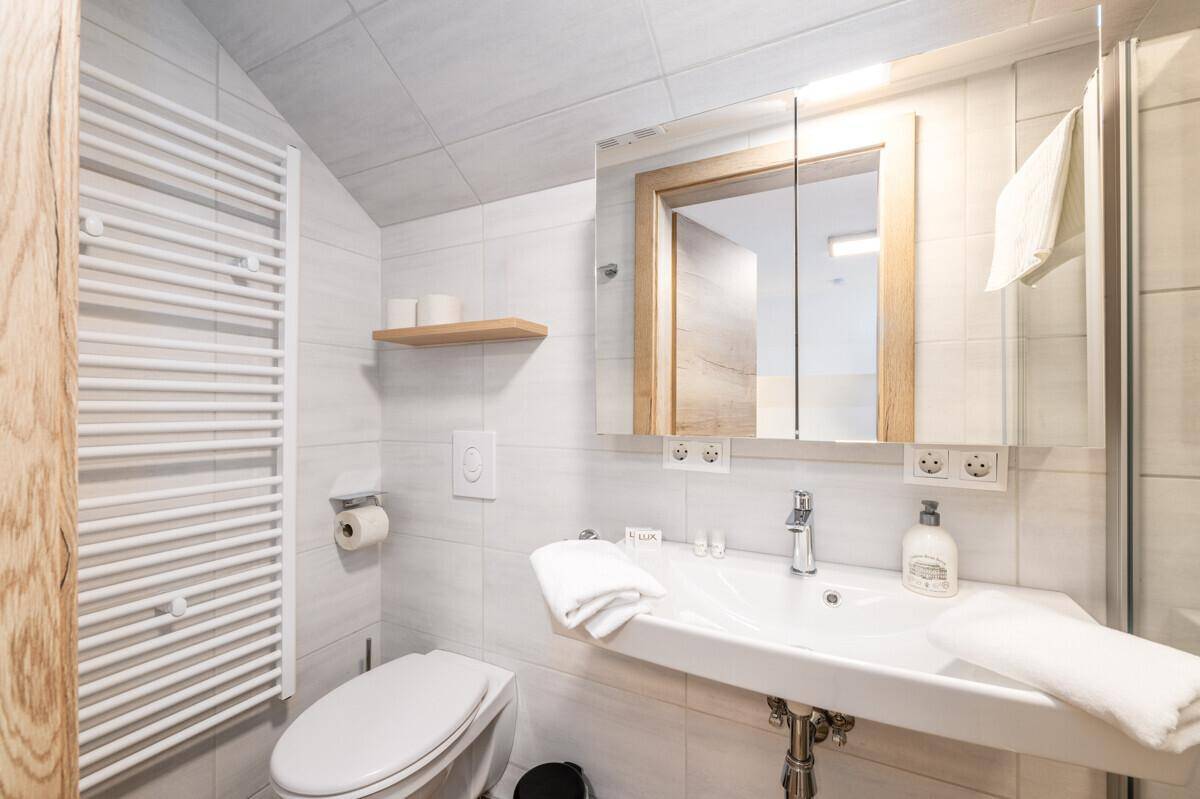 Modernes Badezimmer mit WC, Waschbecken, Spiegel und beheiztem Handtuchhalter.