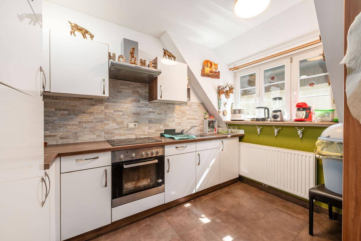 Funktionale Küche mit weißen Schränken, Fliesenboden und einem Fenster unter der Dachschräge.