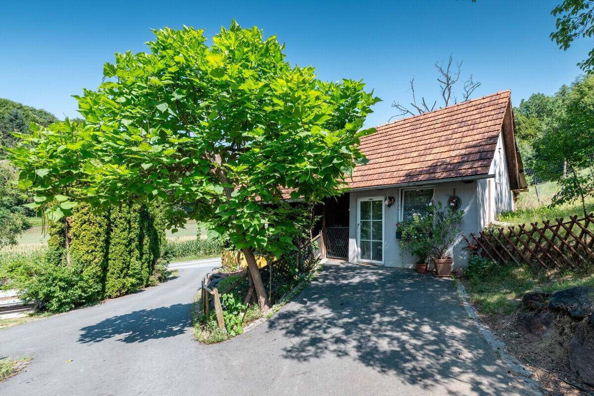 Kleines Haus mit Satteldach und Zufahrt, umgeben von Bäumen und ländlicher Idylle.