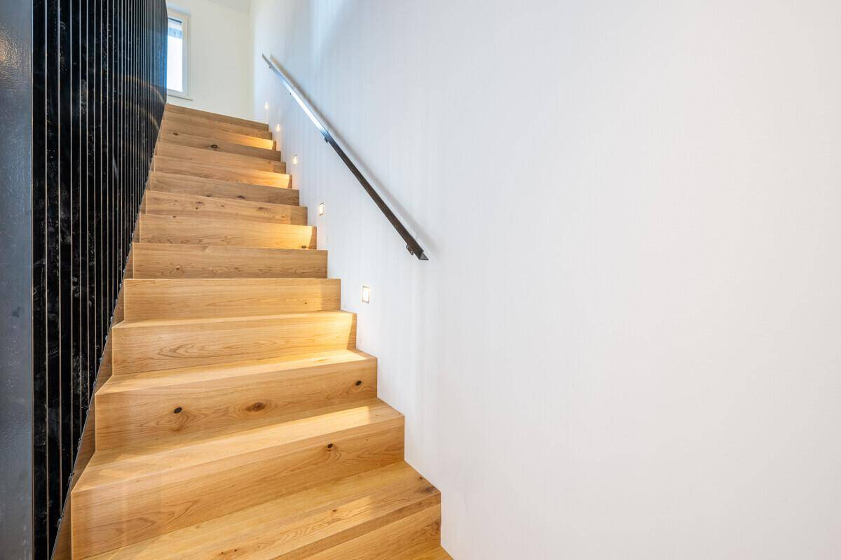 Moderne Holztreppe mit integrierter Beleuchtung und schwarzem Geländer.
