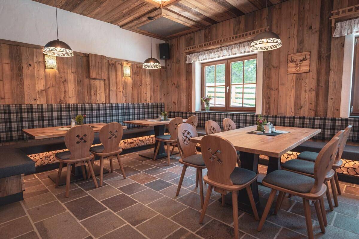 Rustikaler Speisesaal mit Holztäfelung, karierten Sitzbänken und Steinfliesenboden.