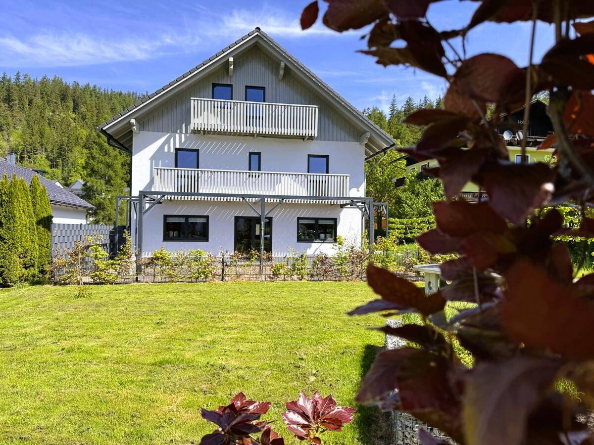 Ruhiger Gartenbereich mit Blick auf das Haus und die umliegende Berglandschaft unter blauem Himmel.