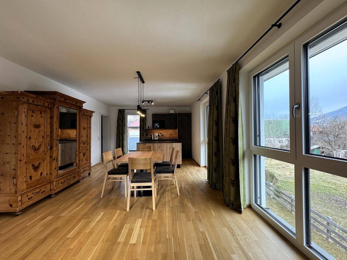 Offener Wohn-Essbereich mit Holzboden, traditionellem Schrank und großen Fenstern.