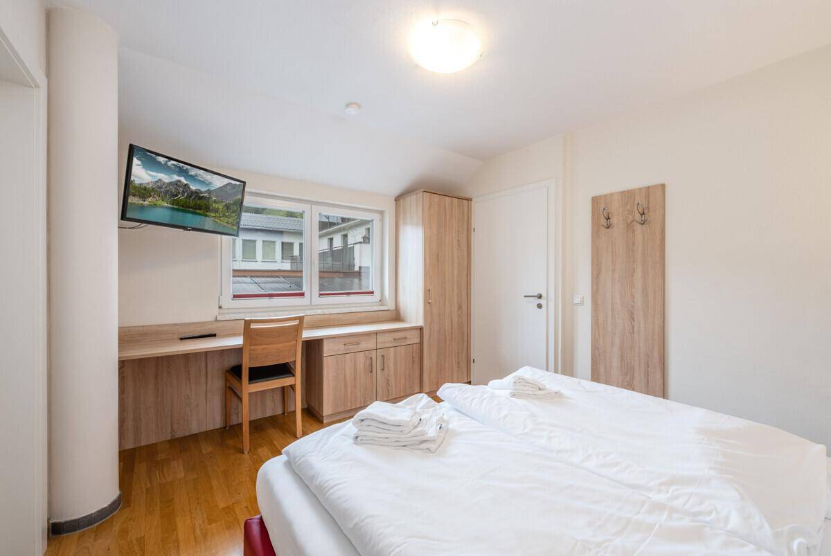 Schlafzimmer mit Doppelbett, Schreibtisch, Kleiderschrank und einem Fenster für Tageslicht.