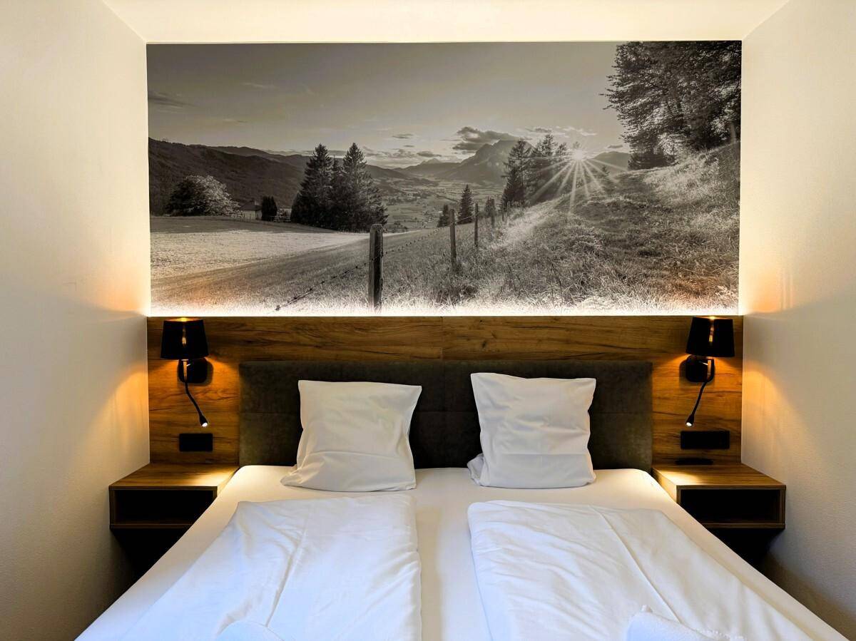 Modernes Schlafzimmer mit Doppelbett, Holzkopfteil und Wandbild mit Landschaftsmotiv.