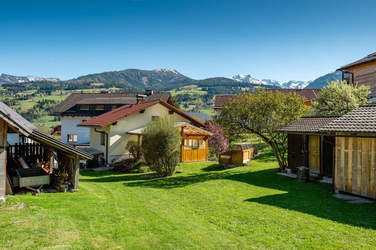 Großer grüner Garten mit Blick auf die Berge und umliegende Häuser, sonnig.