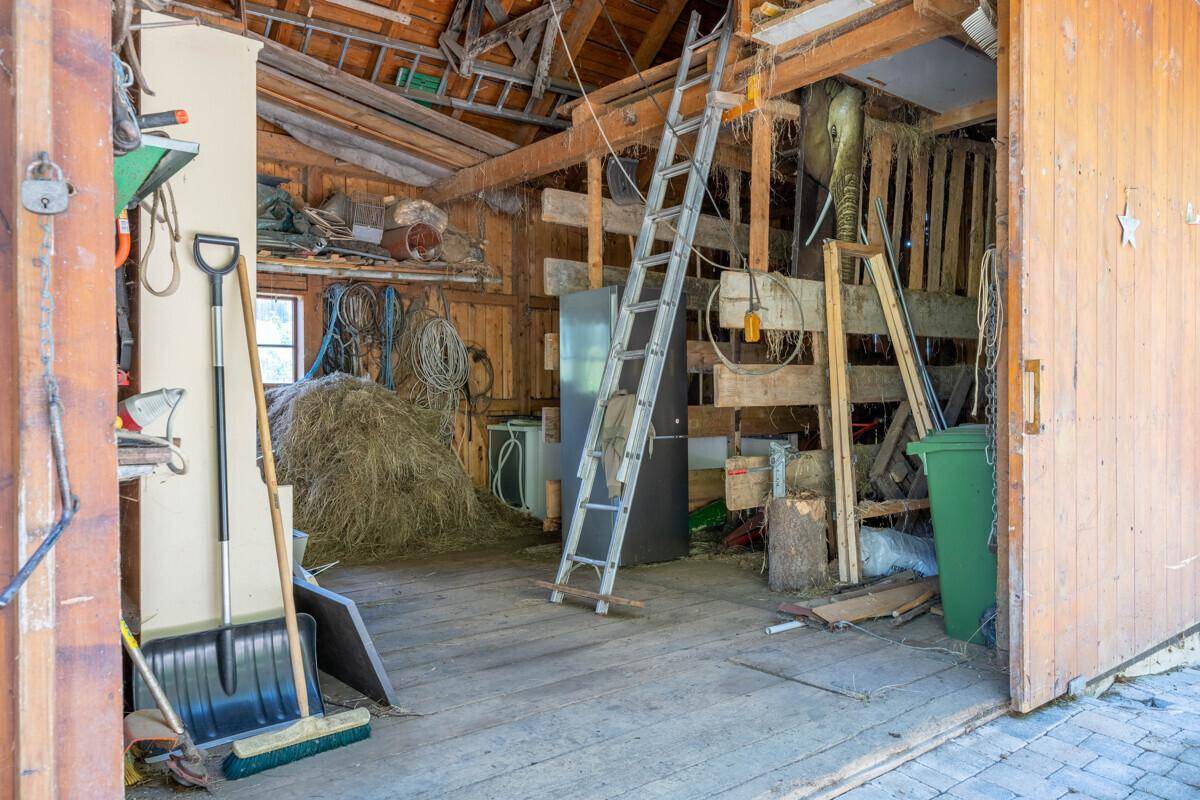 Rustikaler Lagerbereich mit Heu, Leiter und verschiedenen landwirtschaftlichen Geräten.