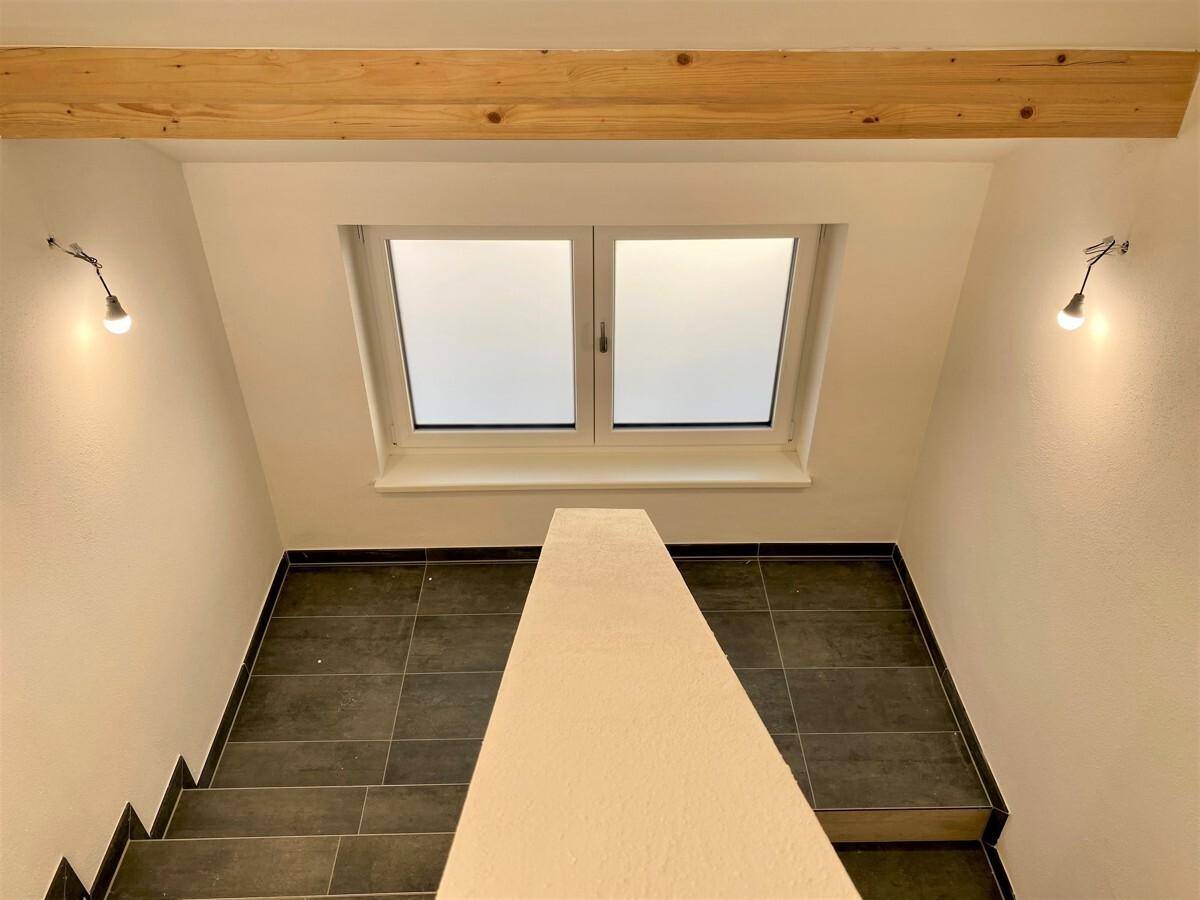 Treppenhaus mit natürlichem Lichteinfall durch ein Dachfenster und Fliesenboden.
