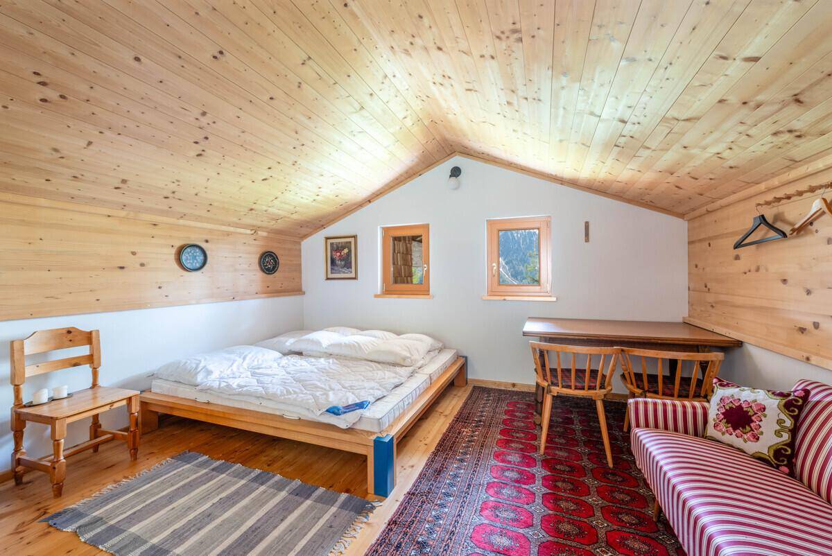 Gemütliches Schlafzimmer im Dachgeschoss mit Holzwänden, schrägen Decken und Fenstern.