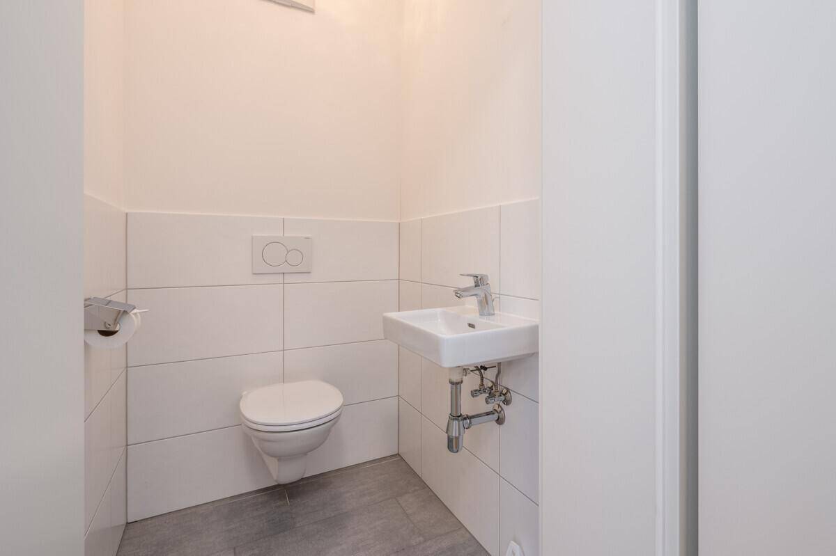 Modernes Gäste-WC mit Wand-WC, kleinem Waschbecken und weißen Fliesen.