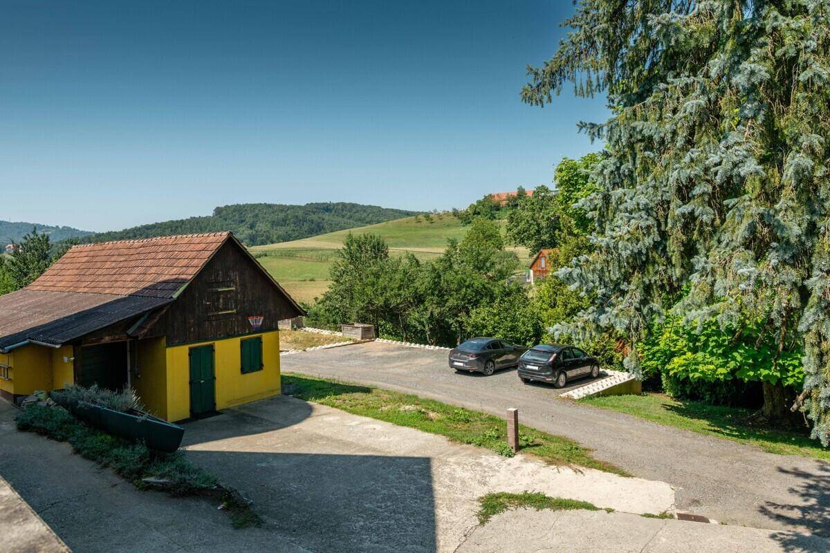 Gelbes Gebäude mit rotem Dach, Parkplätzen und grüner Hügellandschaft im Hintergrund unter blauem Himmel.
