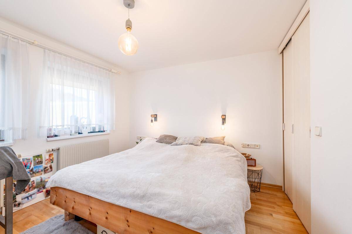 Schlafzimmer mit Holzbettrahmen, weißem Kleiderschrank und hellem Holzboden.