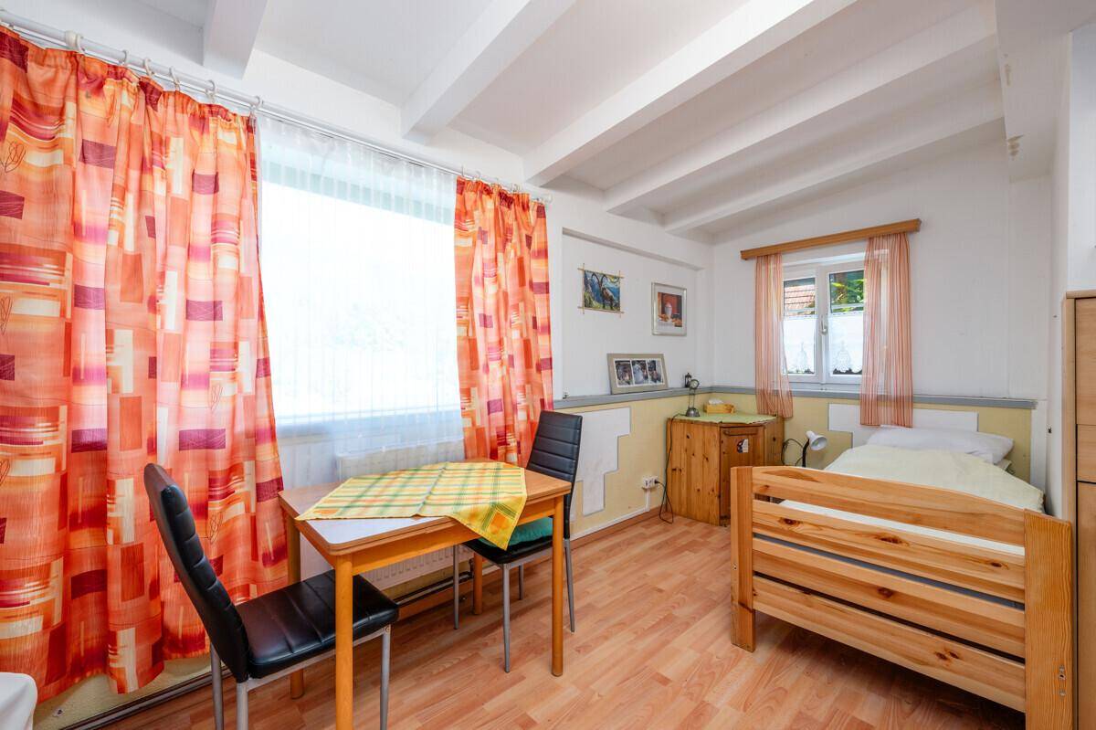 Schlafzimmer mit Einzelbett, kleinem Esstisch und sichtbaren Deckenbalken, hell und freundlich gestaltet.
