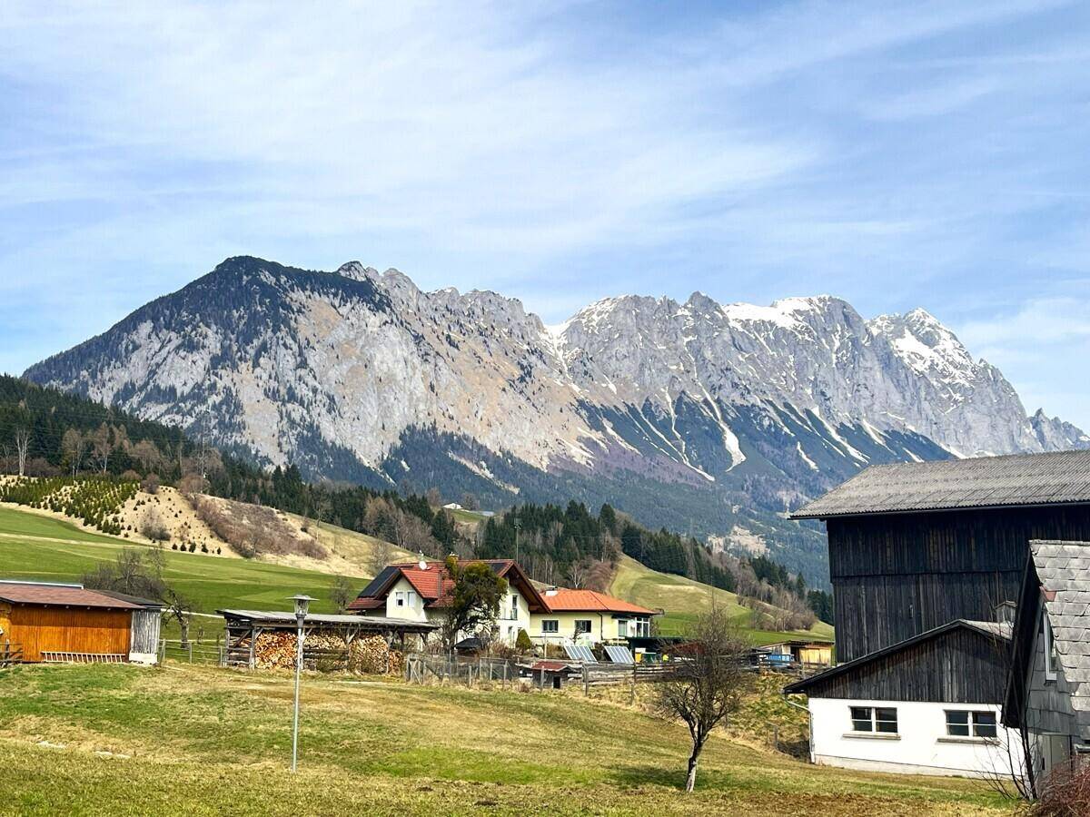 Blick auf eine ländliche Umgebung mit traditionellen Häusern und majestätischen Bergen im Hintergrund.